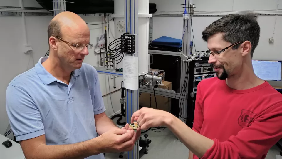 Physics researchers Peter Samuelsson, on the left, and Ville Maisi show the small brass component that contains connectors, microwave circuits and nanowires. PHOTO: SIMON WOZNY