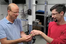 Physics researchers Peter Samuelsson, on the left, and Ville Maisi show the small brass component that contains connectors, microwave circuits and nanowires. PHOTO: SIMON WOZNY